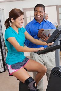 Physical therapist helping teen patient with therapy on exercise bike